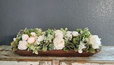 an arrangement of white flowers and greenery in a wooden tray on a table top