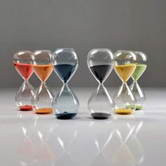 an assortment of different colored sandglasses on a white surface with one hour remaining