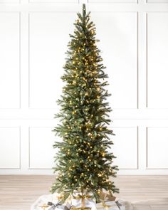 a christmas tree with lights and presents on the floor in front of a white wall