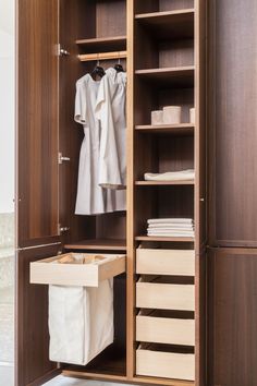 an open closet with clothes hanging on the door and a trash can in front of it