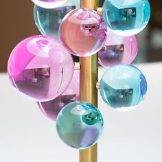 colorful glass balls are hanging from a metal pole in front of a white table top