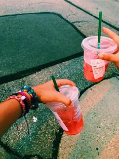 two people holding up drinks in their hands on the side walk, with one person's hand reaching for it