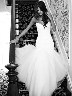 a black and white photo of a woman in a wedding dress standing on stairs with her arms out