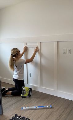 a woman is working on the wall in her room with some paint and tools nearby