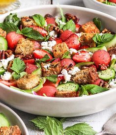 a salad with strawberries, cucumbers and feta cheese in a white bowl