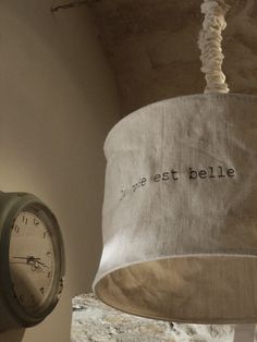 a clock hanging from the side of a wall next to a lamp shade with writing on it