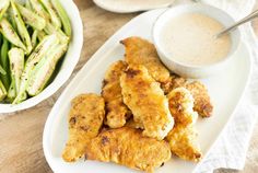 there is a white plate with chicken wings and asparagus next to the bowl