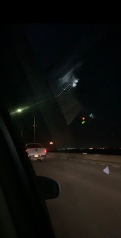 cars driving down the road at night with an airplane in the sky over headlight