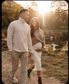 a man and woman walking down a dirt road holding hands while the sun is setting behind them