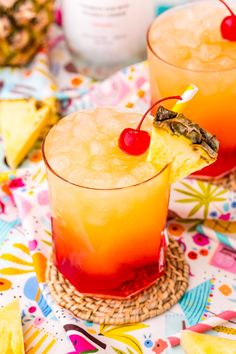 two glasses filled with drinks sitting on top of a table next to pineapples