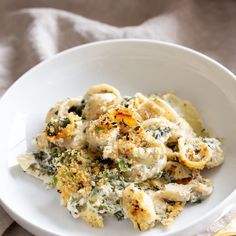 a white bowl filled with pasta covered in cheese and spinach sauce on top of a table