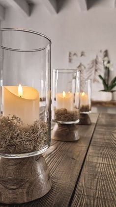 candles are lit in glass vases on a wooden table with moss and succulents