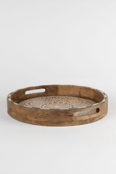 a round wooden tray with handles and holes on the bottom, sitting on a white surface