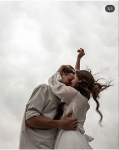 a man and woman are kissing in front of the sky with their arms around each other