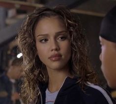 a woman with curly hair is talking to a man in a black jacket and white t - shirt