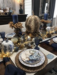 a dining room table set for christmas with blue and white dishes, candles and decorations