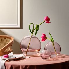 two vases with pink flowers in them on a table next to a chair and wall