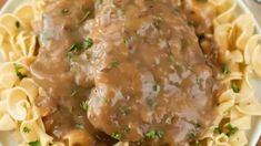 a white plate topped with pasta and meat covered in gravy on top of a wooden table