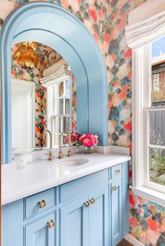 a bathroom with blue cabinets and floral wallpaper on the walls, along with a large mirror