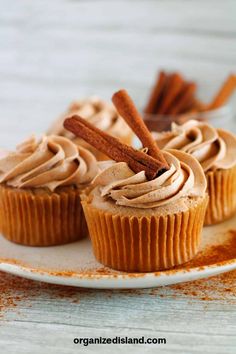 cupcakes with cinnamon butter frosting and cinnamon sticks on top, sitting on a white plate