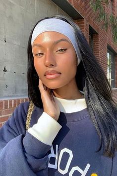 a woman with a headband is standing in front of a brick building and looking at the camera