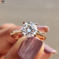 a woman's hand holding an engagement ring with a diamond in the center and two gold bands around it