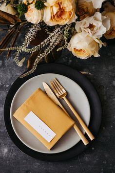 a table setting with flowers and place cards on the plate, along with gold cutlery