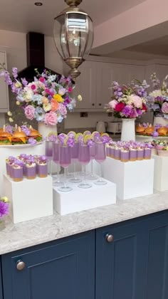 there are many cupcakes on the table with purple frosting and flowers in vases