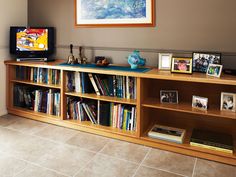 a television sitting on top of a wooden book shelf next to a wall filled with books