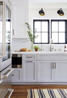 a kitchen with white cabinets, black windows and a striped rug on the wooden floor