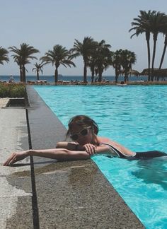 a woman laying on the edge of a swimming pool next to palm trees and water