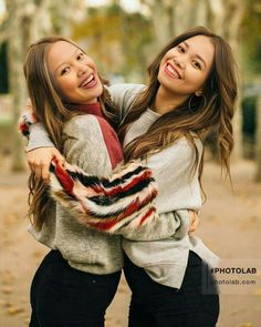 two young women are hugging each other in the fall leaves and smiling at the camera