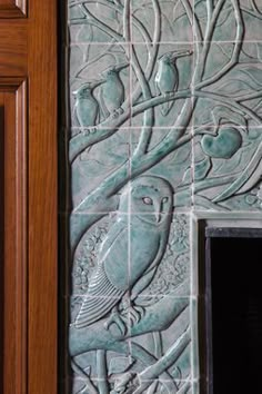 a decorative tile wall with an owl and tree design on the side of it, next to a door