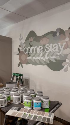 some paint cans are sitting on a table in front of a sign that says come stay