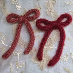 two crocheted bows are sitting on a lace tablecloth, one is red and the other is white