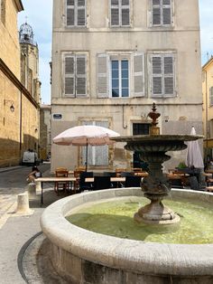 an outdoor fountain in front of a building with tables and umbrellas on the ground