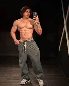 a shirtless man taking a selfie with his cell phone while wearing sweatpants