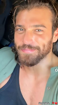 a man with long hair and beard sitting in a car looking at the camera smiling