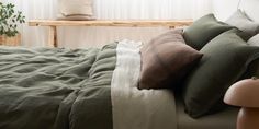 a bed with green sheets and pillows on top of it next to a wooden bench