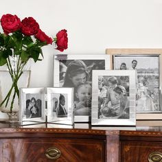 some pictures and flowers on a dresser with red roses in vases next to them