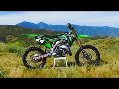 a green dirt bike parked on top of a grass covered field with mountains in the background