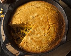 a cornbread cake in a cast iron skillet on a wooden table with a slice cut out