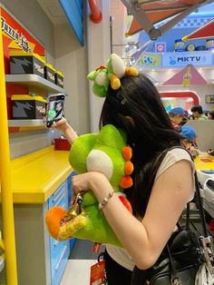 a woman looking at her cell phone while holding a stuffed frog in front of a toy store shelf