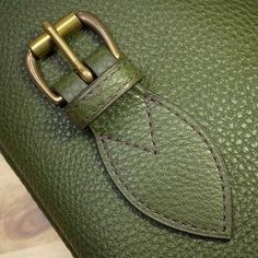 a green leather bag with a gold buckle on the front and side, sitting on a wooden surface