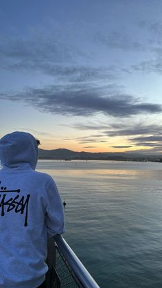 a person wearing a hoodie looking out over the water at sunset on a boat