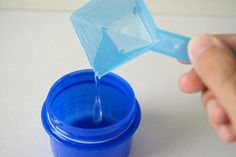 a person is pouring blue liquid into a plastic cup with a spoon in the other hand