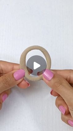 two hands holding a wooden ring with pink nail polish on it and one hand pulling the ring