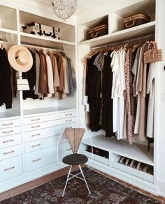 an organized closet with white cabinets and hanging clothes on hangers, a chair in the foreground