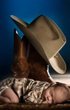 a baby wearing a cowboy hat laying on the ground next to a pair of boots