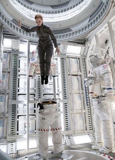 two astronauts in space suits and one is standing on a platform with his arms outstretched